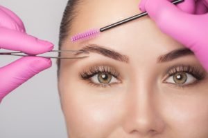 Makeup artist plucks eyebrows with tweezers to a woman before staining with henna. Cosmetology concept