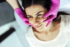 Cosmetologist examining facial wrinkles on young woman face